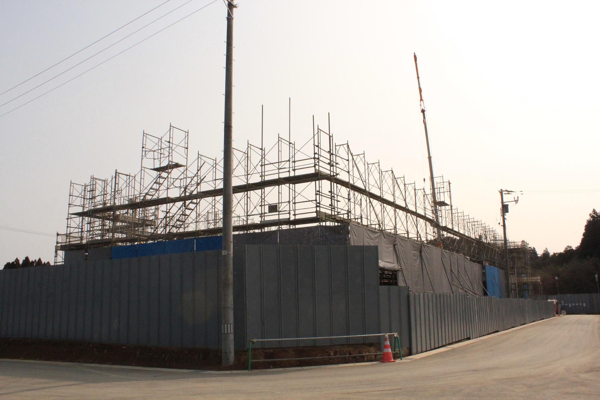グレーの仮囲いの奥に足場が組まれ、クレーンが高く伸びている大規模な建設現場の写真