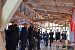 木造の骨組みができた建築中の家の中で、スーツ姿の参加者たちが一斉に手に持ったお神酒に口をつけている様子の写真