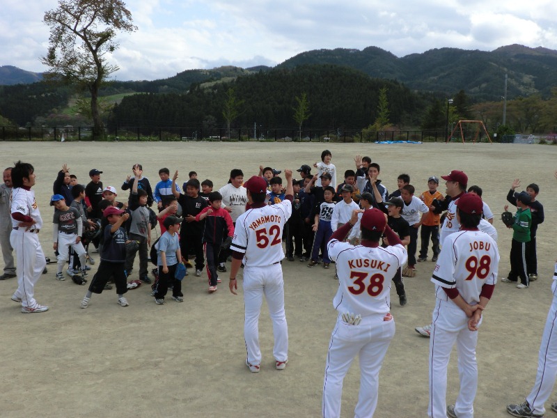 広々としたグランドにユニフォーム姿の楽天イーグルスの選手の皆さんと子ども達が集まり、一人の選手対子どもたち全員でじゃんけんをするなど、和気あいあいと交流している楽天ふれあい教室の様子を捉えた写真