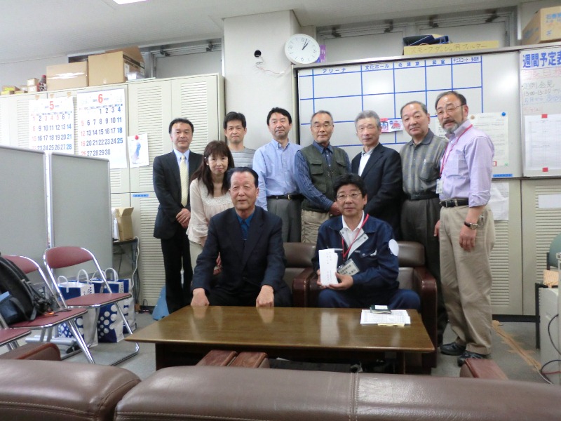 町長が義援金の白い封筒を手に中央の椅子に座り、志津川高校旧職員有志の会の皆さんと一緒に写っている記念写真