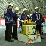 トンネル内で、リボンで飾られ1と書かれた台の上に酒樽が置かれ、頭にヘルメットを被り、木槌を持った法被姿の4人の人達が鏡開きを行っている様子の写真