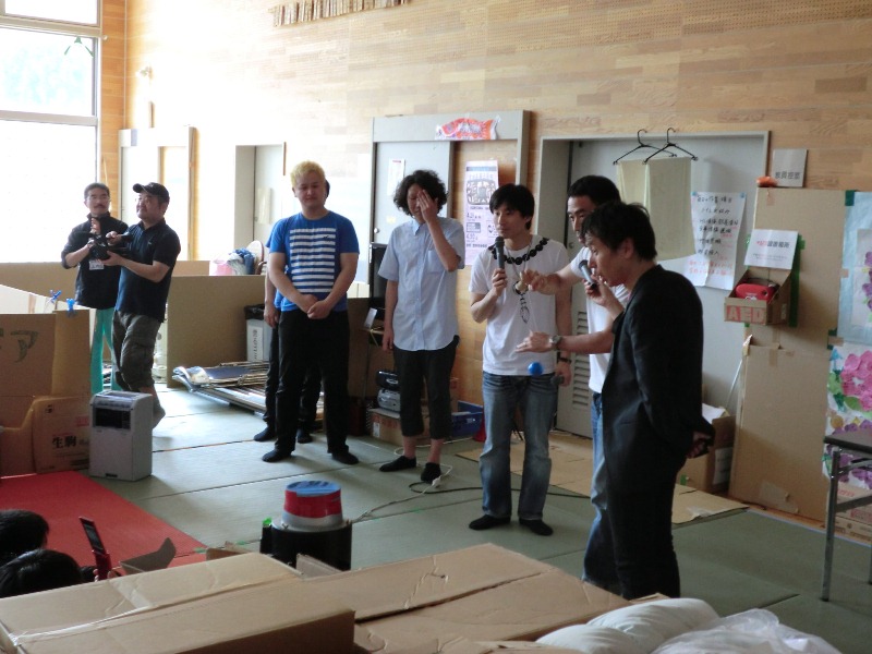 避難所で、吉本興業の芸人の皆さんが被災者を元気づけるために訪問し、マイクを持って話をしている様子を写した写真