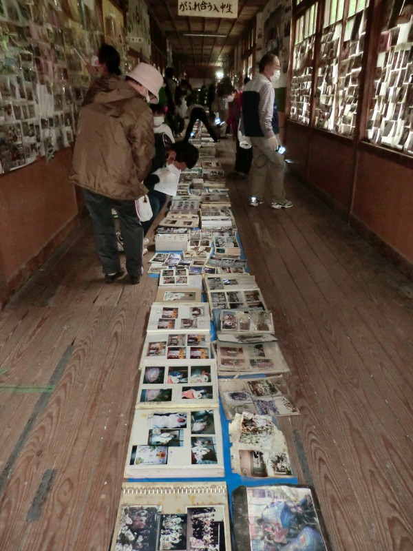 多数のアルバムや写真が床一面に並べられ、壁が窓にもたくさんの写真が貼られ、訪れた人々が写真を確認し見ている様子を写した写真