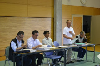 席を立った熊谷健一さんが資料を手に持ち、話をしている様子の写真