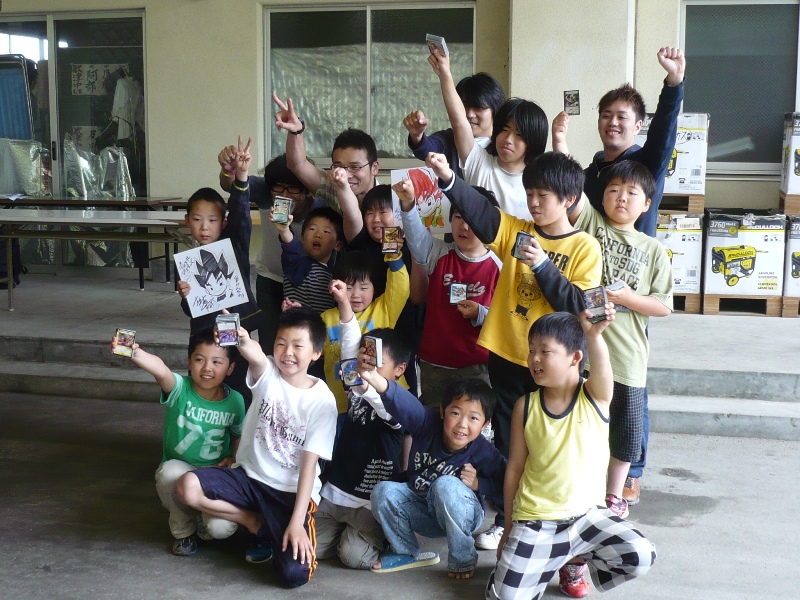 カードやイラストが描かれた色紙を手にもって見せ、笑顔で写っている子どもたちの集合写真