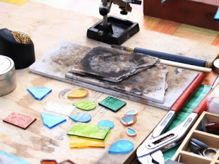 色とりどりのガラス片や道具が並べられた作業台で、ガラス工芸の制作途中の様子を写した写真