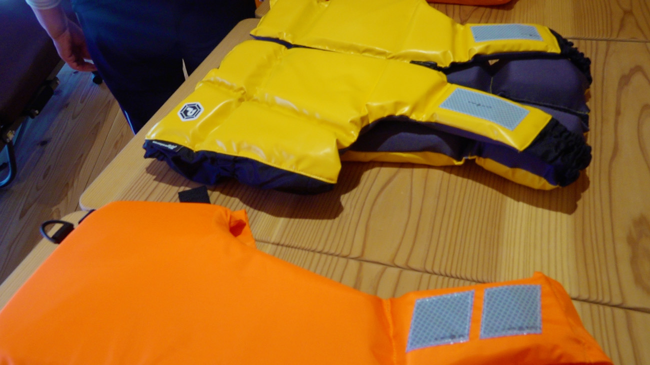 テーブルの上に黄色とオレンジ色のライフジャケットが並べられた写真