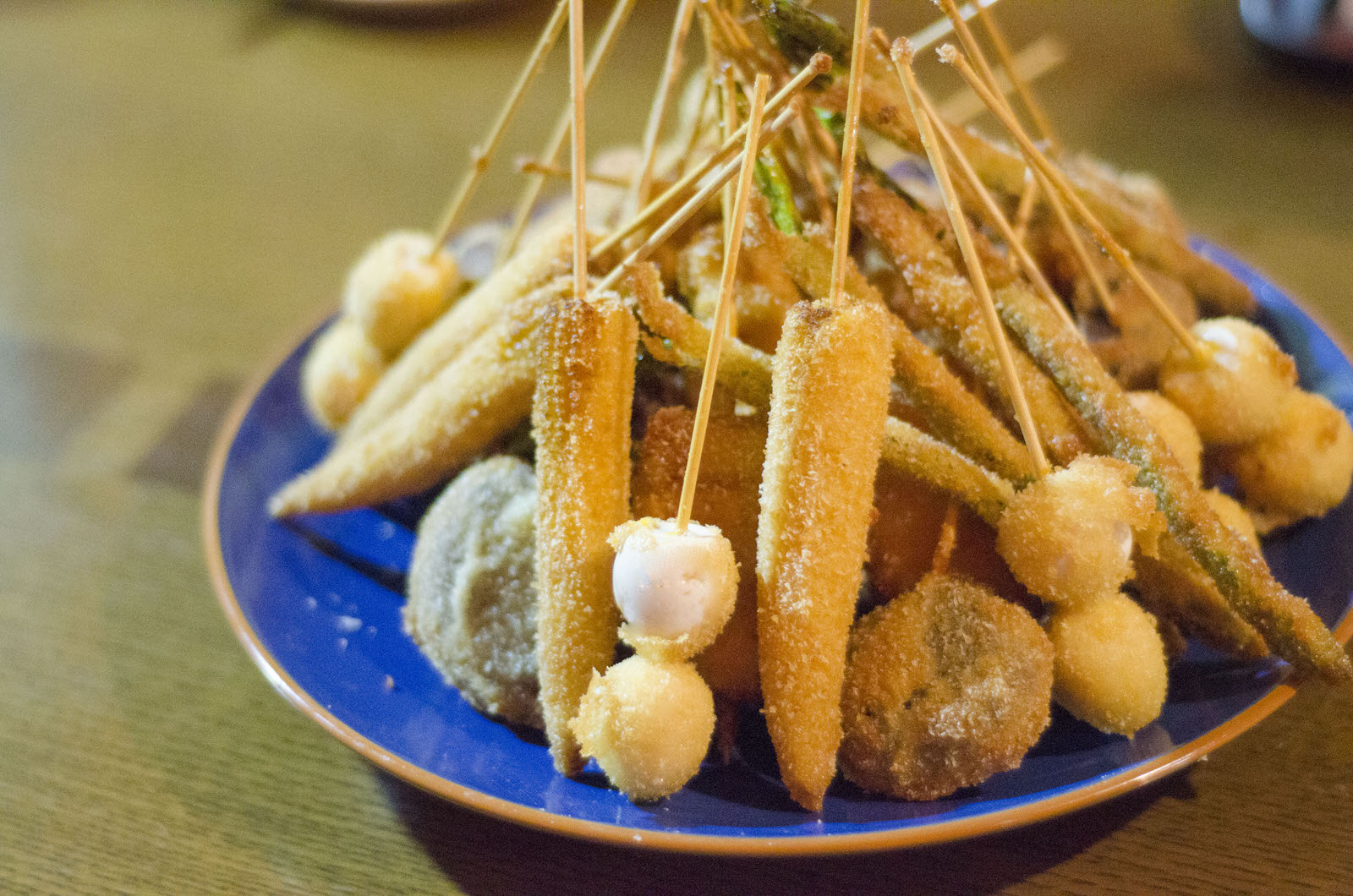 青い皿にうずらの卵や様々な野菜などを使ったたくさんの串カツが山のように盛り付けられている写真