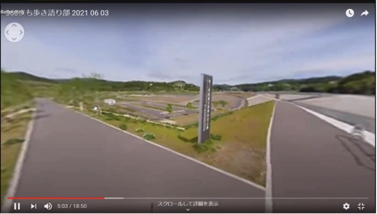 中央に縦長の案内看板が立っている場所を境に、二股に分かれた舗装された遊歩道と、奥に植栽が整備された広い震災復興祈念公園が写っているスクリーンショット画像