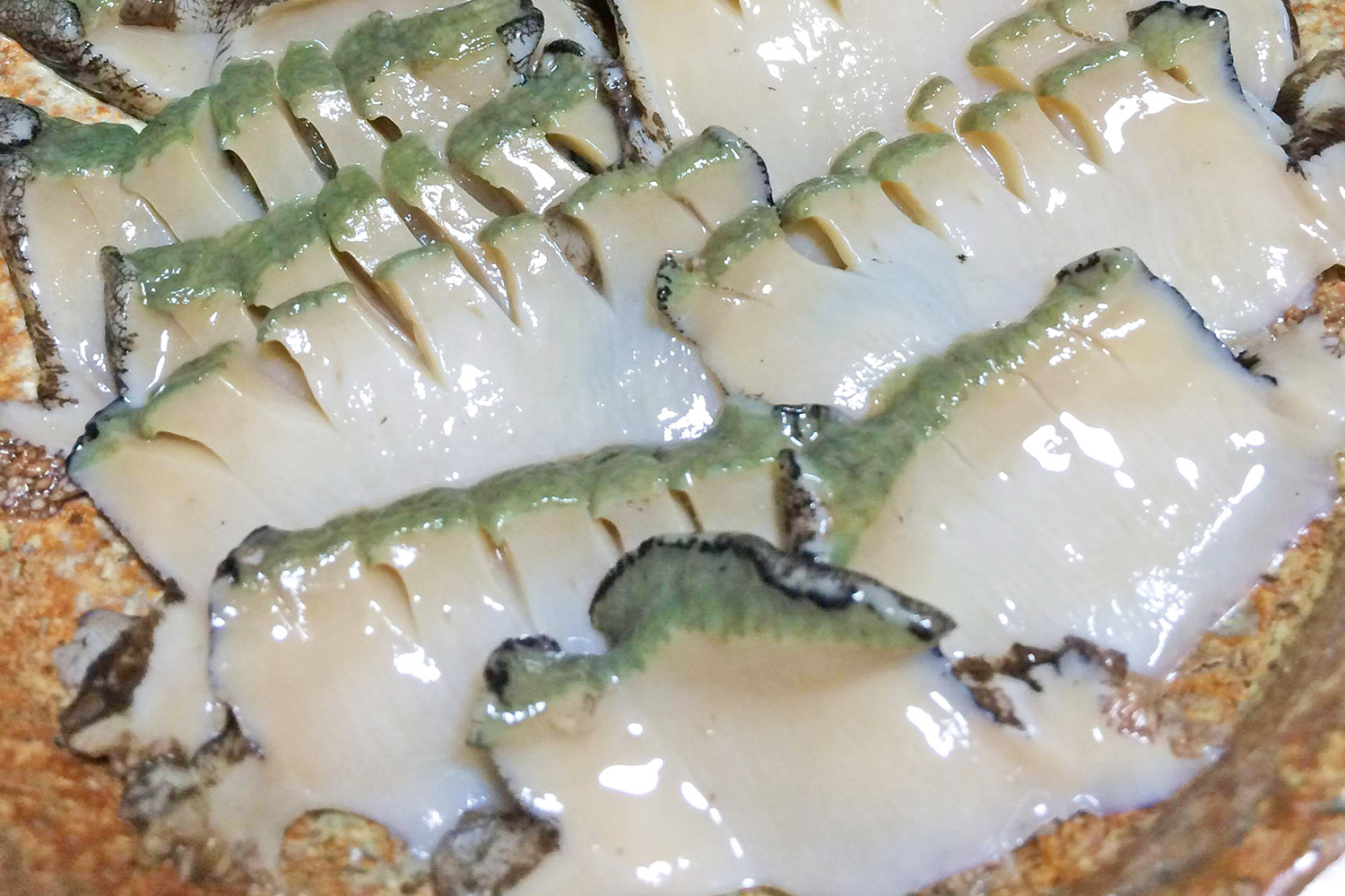 茶色い皿に身は白くて光沢があるアワビの刺身が並んでいる写真