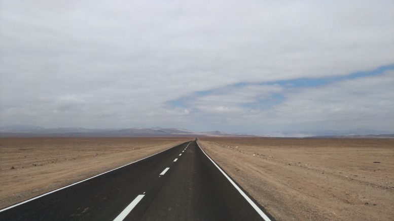 まっすぐに延びる黒い舗装道路が、広大で乾燥した砂漠の中を走っている写真