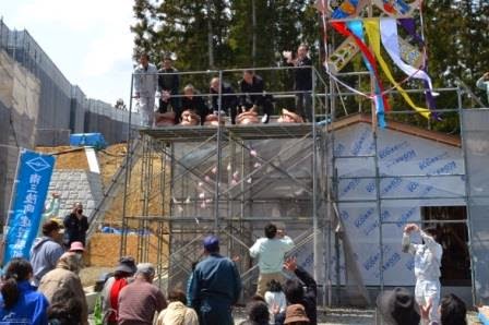 足場の上の人々が餅が入った袋を投げ、それを拾おうと多くの人々が下で両手を挙げている賑やかな餅まきの様子の写真