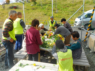 黄色いベストを着用し屋外の大きなテーブルを使い花を仕分けている写真