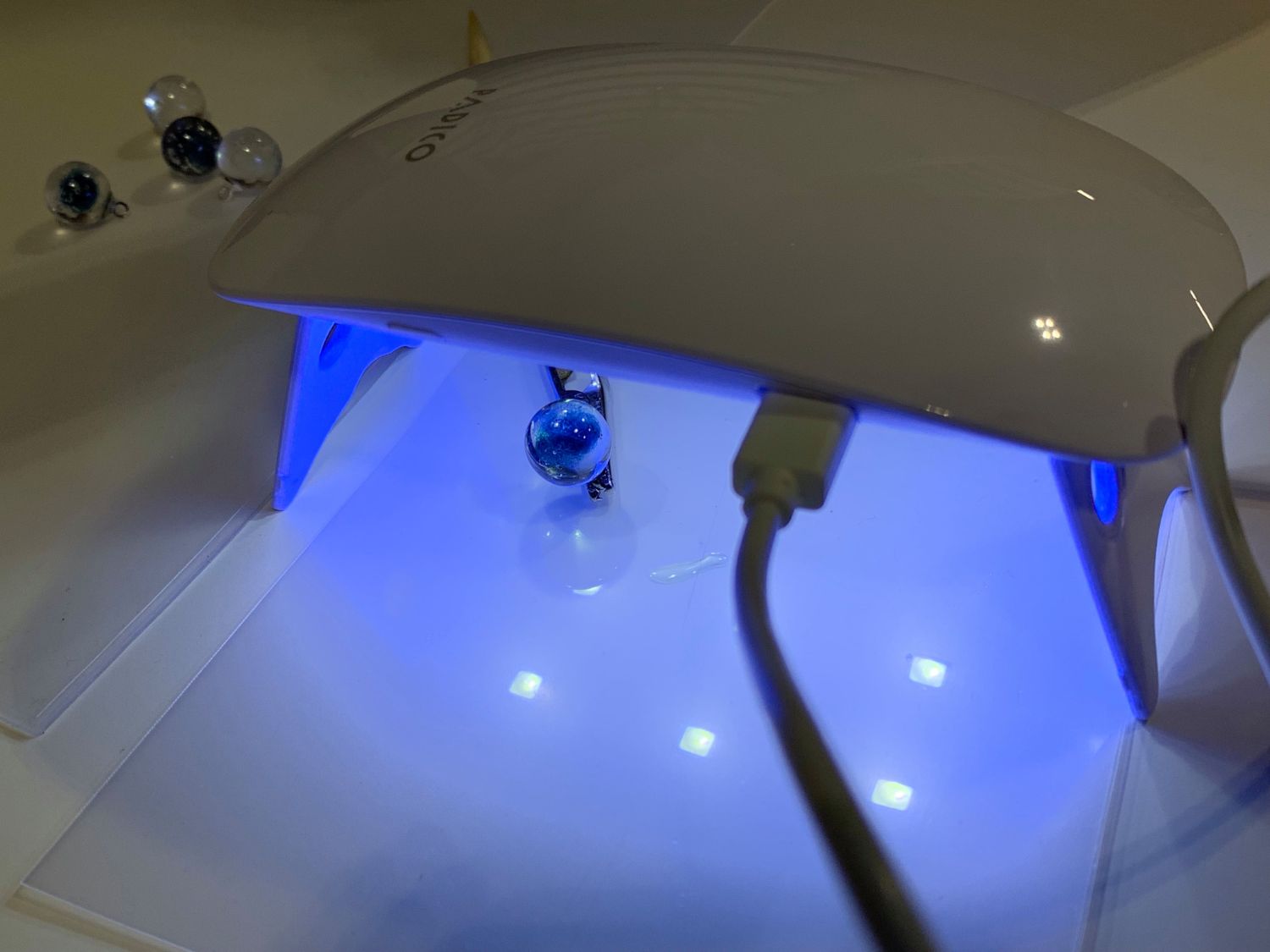 青いガラス玉がUVライトの下に置かれ、硬化処理が行われている様子の写真