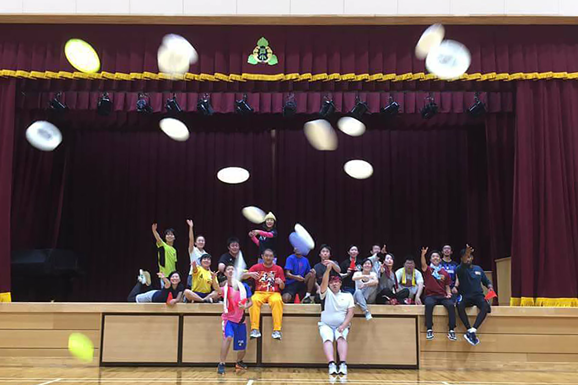 ステージ上に並んで座っている人たちが、カメラに向かってフリスビーを投げている写真