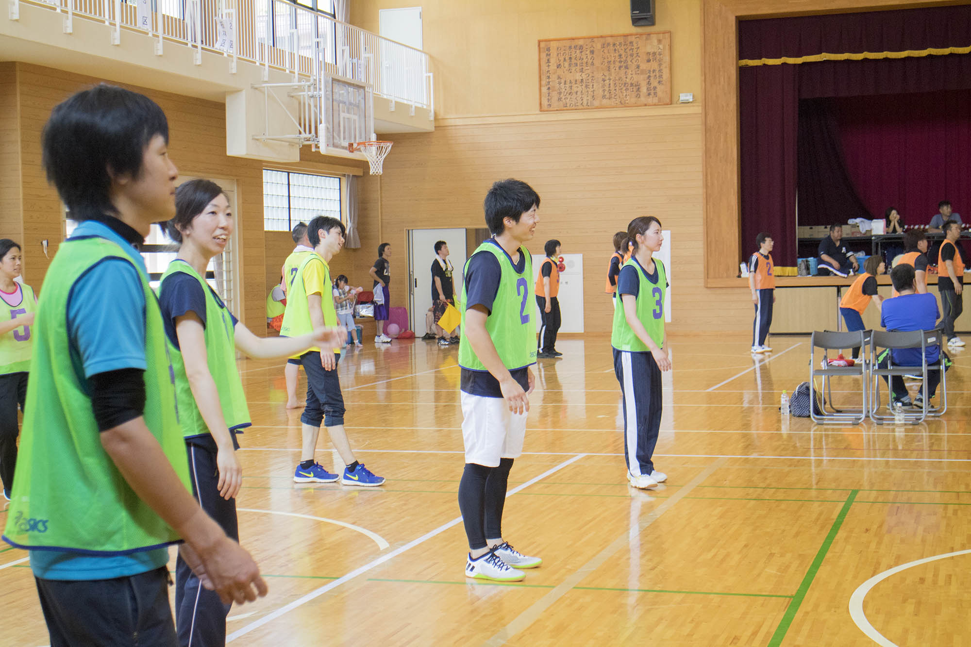 体育館で緑色のビブスを着た複数の選手がコート内に入並んでいるいる様子の写真