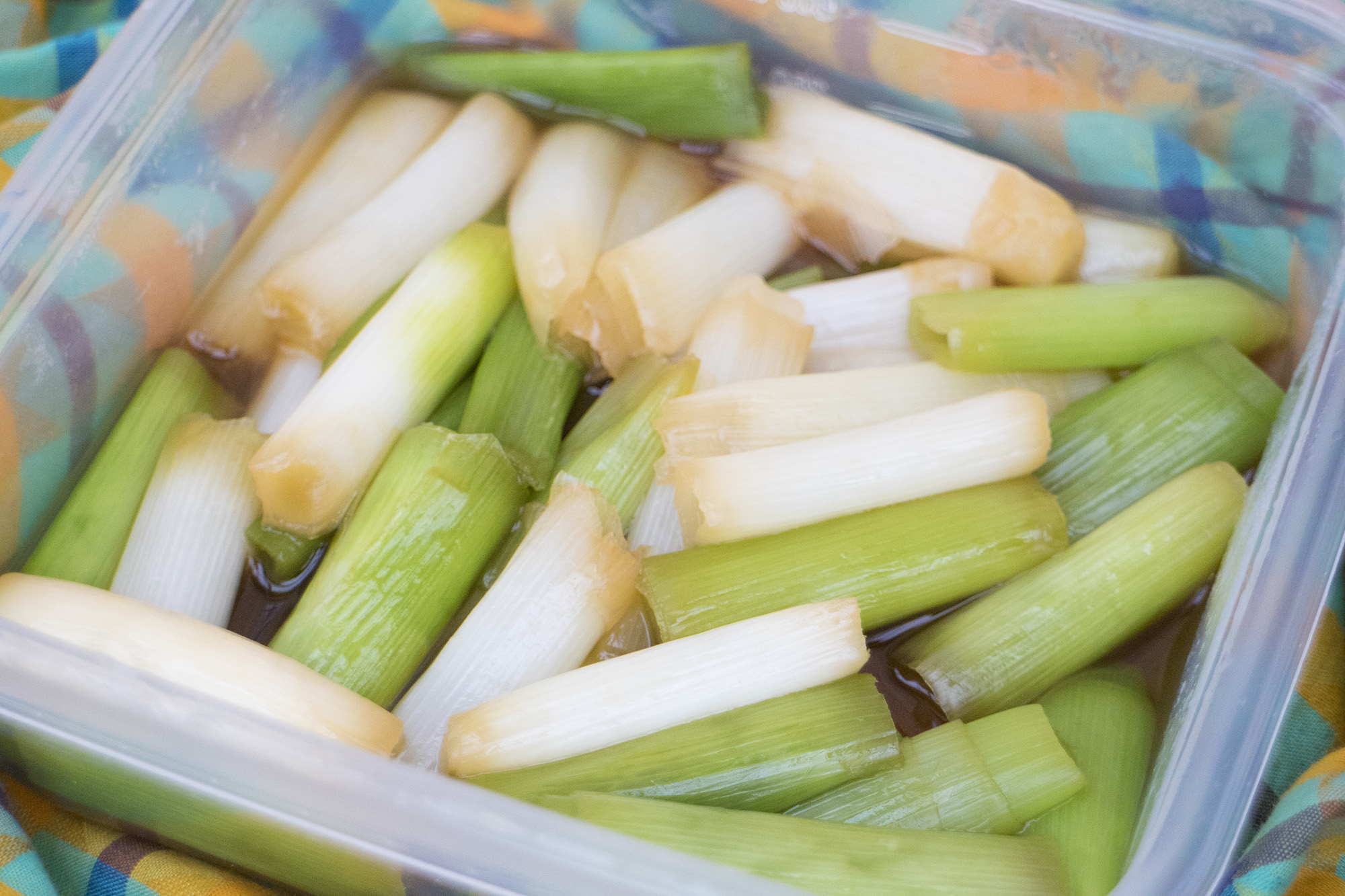 透明のフードコンテナにぶつ切りにしたネギがたれに漬かった料理が入っている写真