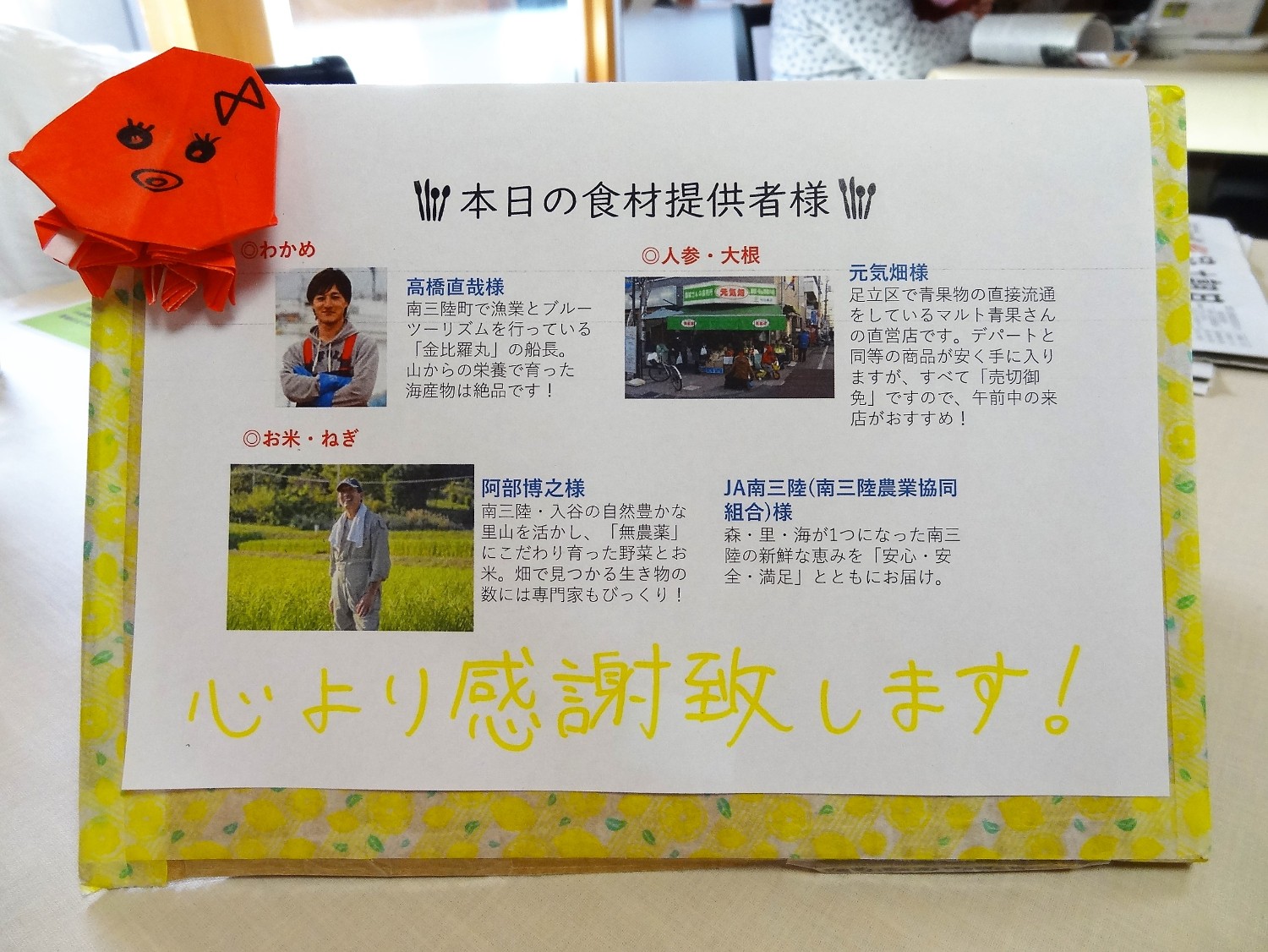 「本日の食材提供者様」と題された掲示物に、わかめ・人参・大根・お米・ねぎの提供者として高橋直哉様、元気畑様、阿部博之様、JA南三陸様の名前と、それぞれの食材の特徴や育て方へのこだわりが丁寧に紹介されている写真