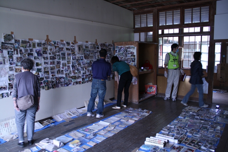 室内の床や壁にたくさんの写真が並べて展示され、来場者が写真の前に立ち止まり、見入っている思い出の写真展示会の様子を写した写真