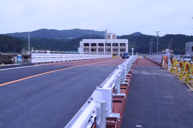 青い空の下、山々を背景に水尻橋の新しい仮橋が完成し、車が通行している様子を写した写真