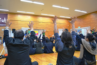 体育館で演奏を聴いている観客が手を上げて盛り上がりながらライブを楽しんでいる様子の写真