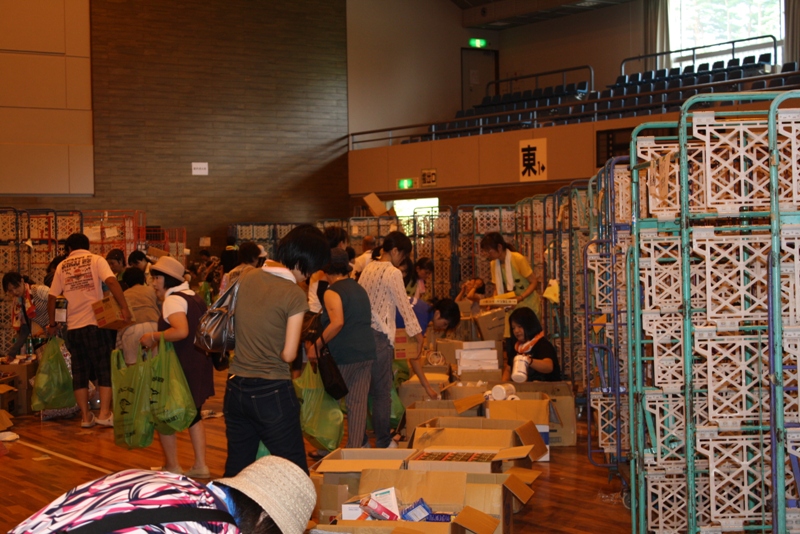 体育館内で、たくさんの人が段ボールやカゴに並んだ品物を見ながら買い物を楽しんでいるフリーマーケットの様子の写真