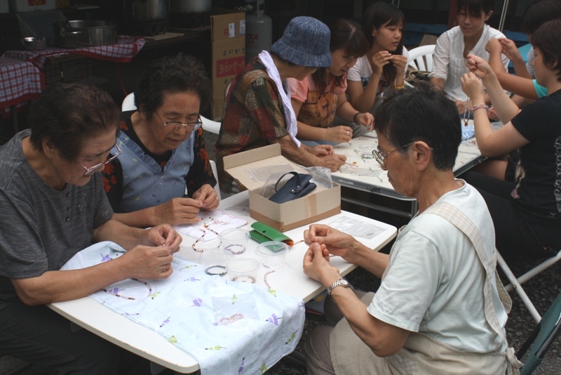 テーブルを囲んで、参加者の皆さんがビーズを使ったアクセサリー作りに集中して取り組んでいる様子の写真