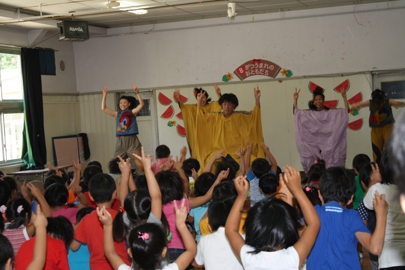 Earth-Beのダンサー5名が前方で踊り、たくさんの子どもたちが一緒に手を上げて楽しそうにダンスしている様子の写真