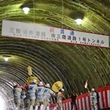 「祝 貫通 三陸沿岸道路 南三陸道路1号トンネル」と書かれた大きな横断幕、両側に紅白幕が掲げられたトンネル内で、白い帽子にお揃いの服を着用した人たちが神輿を担ぎ、大きな団扇をふっている樽みこしの写真