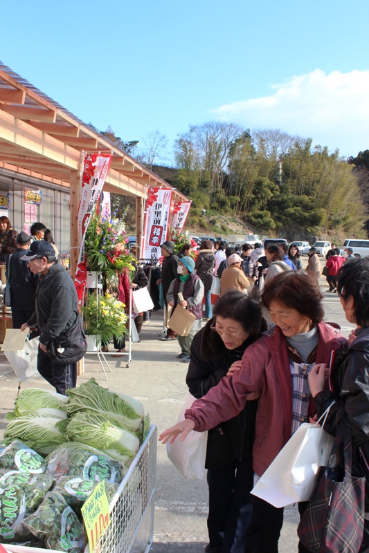 かごに並んだ白菜やホウレンソウを見て笑顔を見せる来場者たちの姿が写る、伊里前福幸商店街オープンの様子の写真