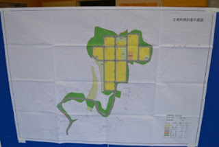 区画が黄色と緑色に整然と色分けされている桝沢団地の土地利用計画図が壁に掲示されている様子の写真