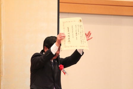 佐藤町長が表彰状を高く掲げて受賞の喜びを示している様子の写真