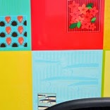 背景が4つの色分けされた区画に分かれており、上は赤色のツツジの花と緑の葉、下は水色でサンマが描かれているデザインをアップで写した写真