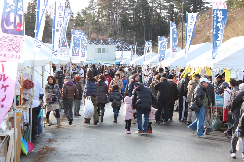 会場にはたくさんのテントが並び、色とりどりの旗が風になびくにぎやかな復興市の会場で、多くの人が買い物を楽しんでいる様子の写真