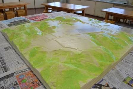 地形模型に緑色の塗料を塗って山や森林の起伏を表現し始めた初期段階のまちづくり模型の写真