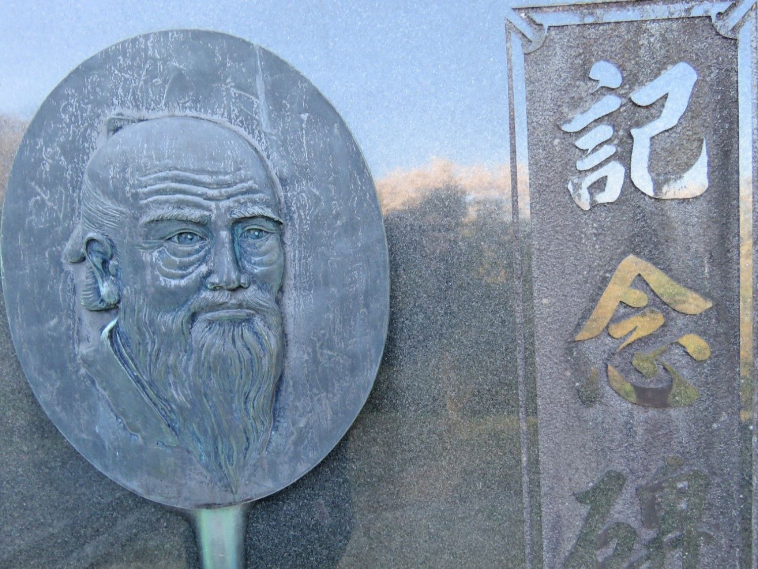 髭を生やした山内甚之丞の顔がレリーフ状に彫られた楕円のプレートと、右に縦書きで「記念碑」と刻まれた黒い石碑が写っている写真