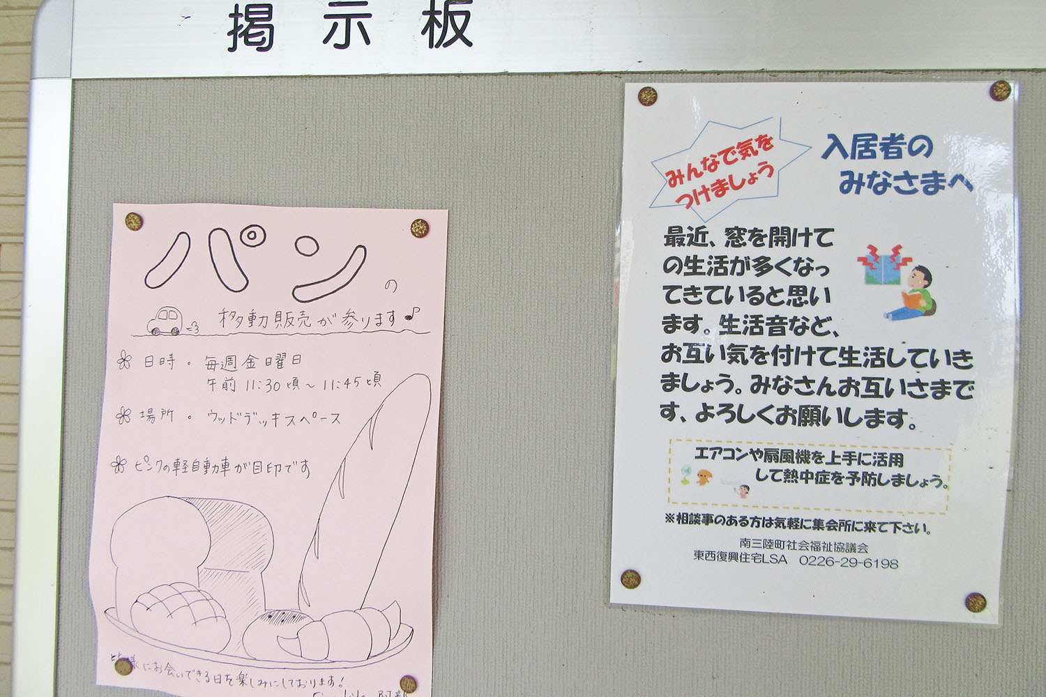 手書きのパン移動販売のお知らせと、生活音への配慮を呼びかける注意書きが並んで掲示板に貼られている写真