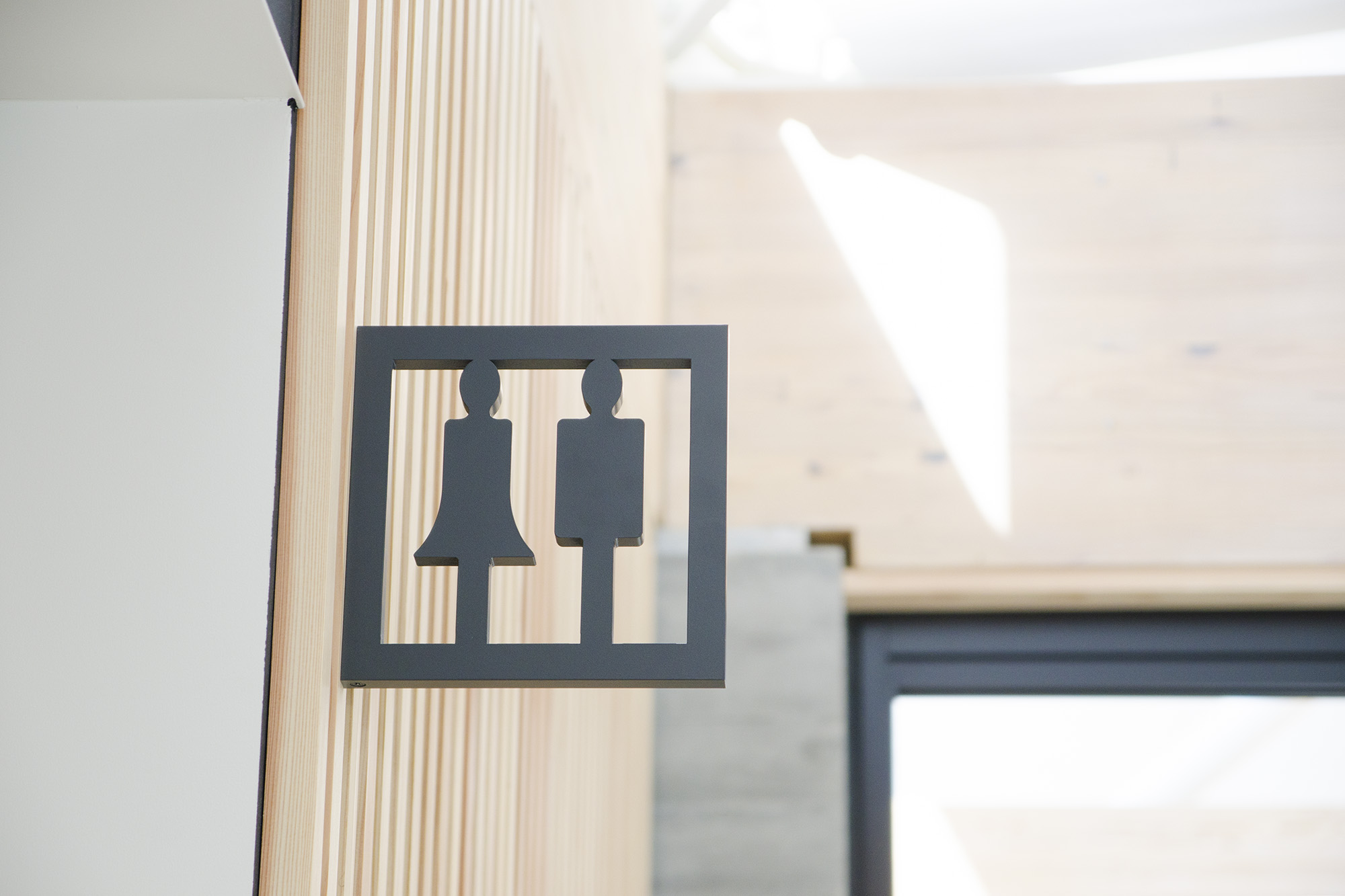 木の壁に設置された、黒いシルエットで男女の形を表すデザインのトイレ案内表示板がアップで写されている写真