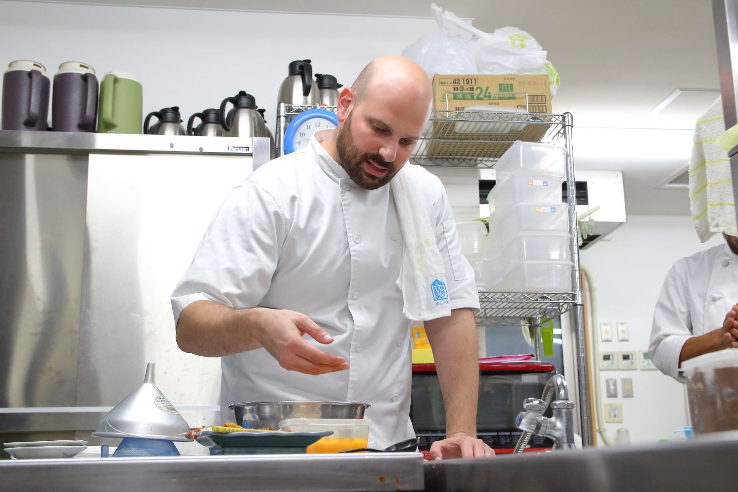 白いコックコートを着用したイスライル・シャーさんが真剣な表情で料理を作っている様子の写真