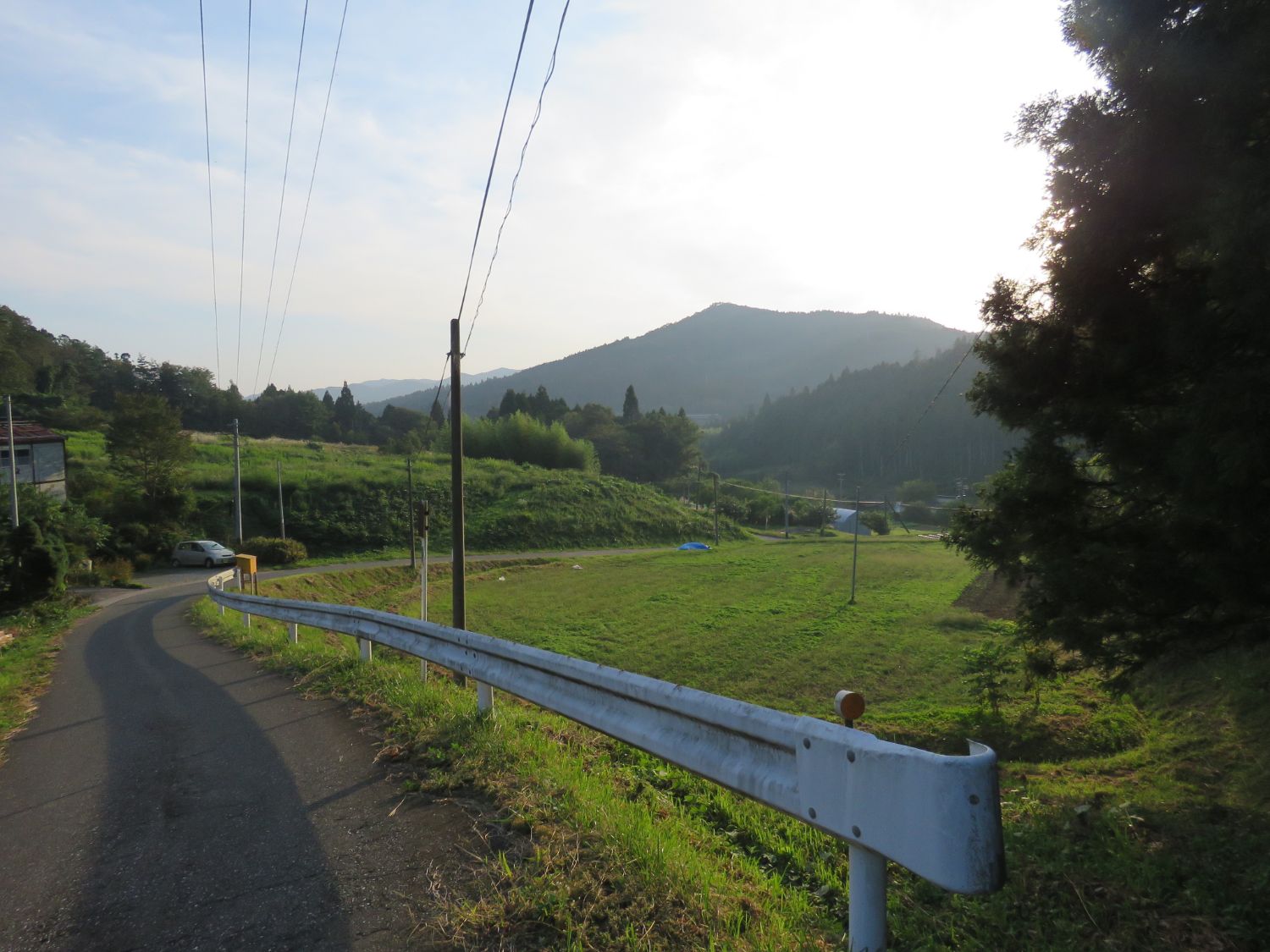 緩やかなカーブを描いた坂道と広々とした田園風景の写真