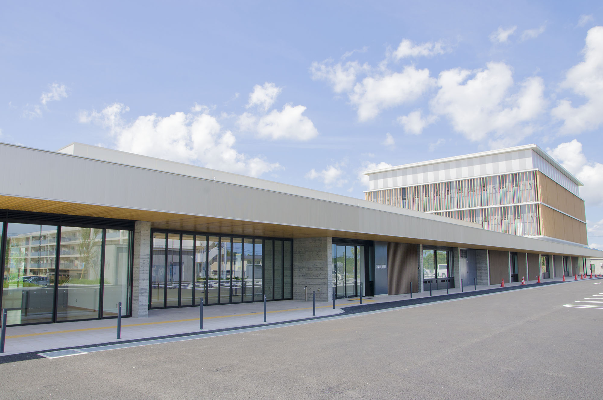 青空の下、水平に長く伸びるガラス張りの低層部分と、木目調の縦格子が特徴的な四角い高層部分からなる、シンプルで現代的なデザインの南三陸町役場新庁舎の写真