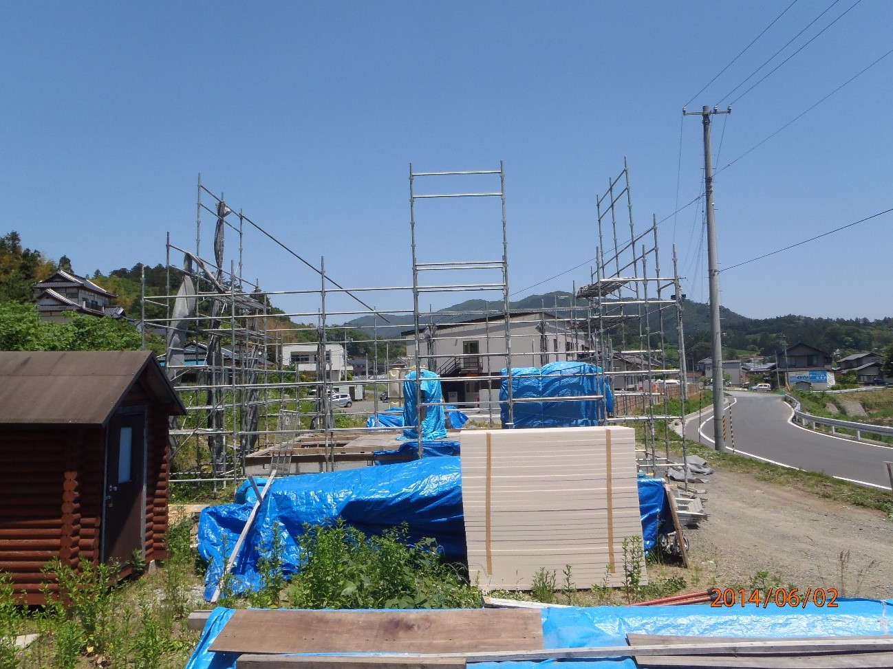 建設中の建物の骨組みがむき出しになっており、周囲には青いシートで覆われた資材が置かれている工事現場の様子を写した写真