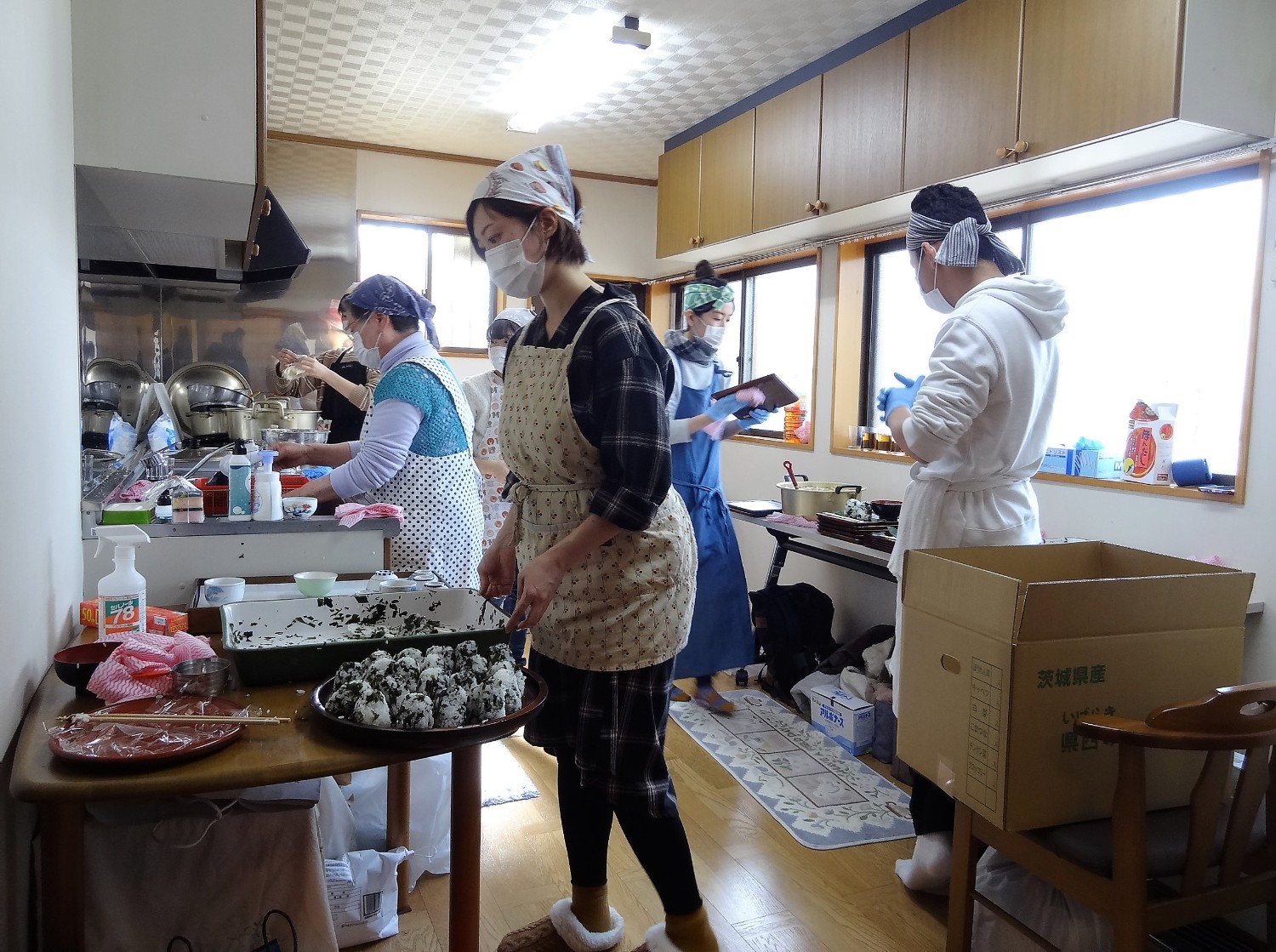 数人の人々がエプロンを着けて広々としたキッチンに立ち、それぞれの作業を行っている様子の写真