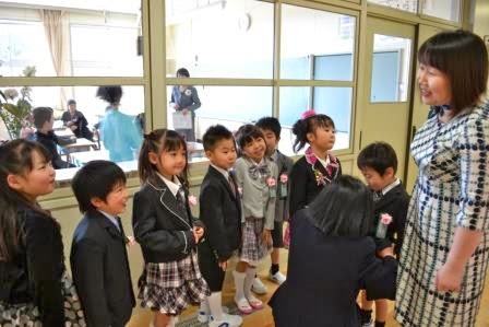 式が終了し安心した表情の児童たちが廊下で女性教師の話を聞いている写真