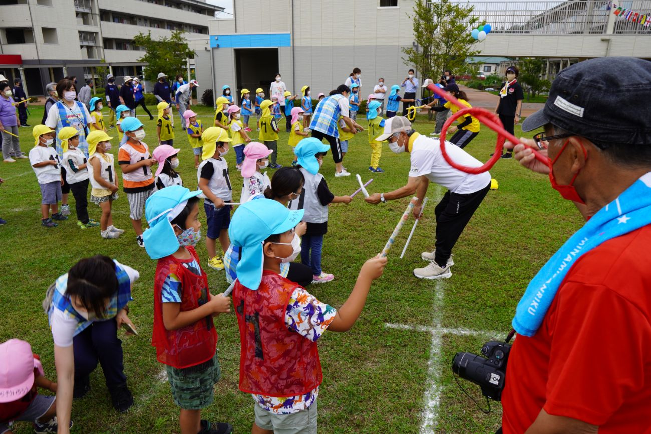 チームごとに列になった子どもたちが、手に持った棒で、先頭の大人たちから輪っかを受け取っている様子の写真