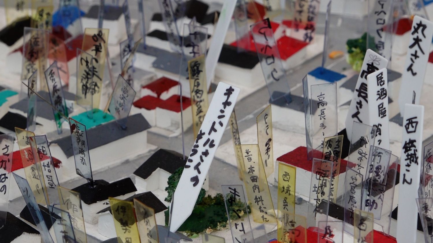 小さな家々の模型の上に、多数の透明なプレートが立てられ、それぞれに人名が手書きされている写真