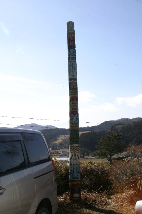 色鮮やかな顔や模様が刻まれた非常に背の高いトーテンポールが、青空の下の屋外に立っている風景写真