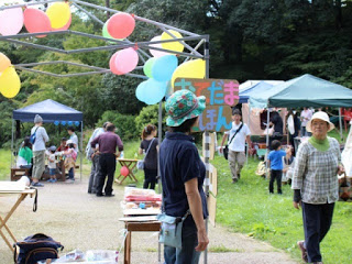 色とりどりの風船が吊るされたテントの下で、子ども向けの遊びコーナーが開かれており、人々が楽しんでいる写真