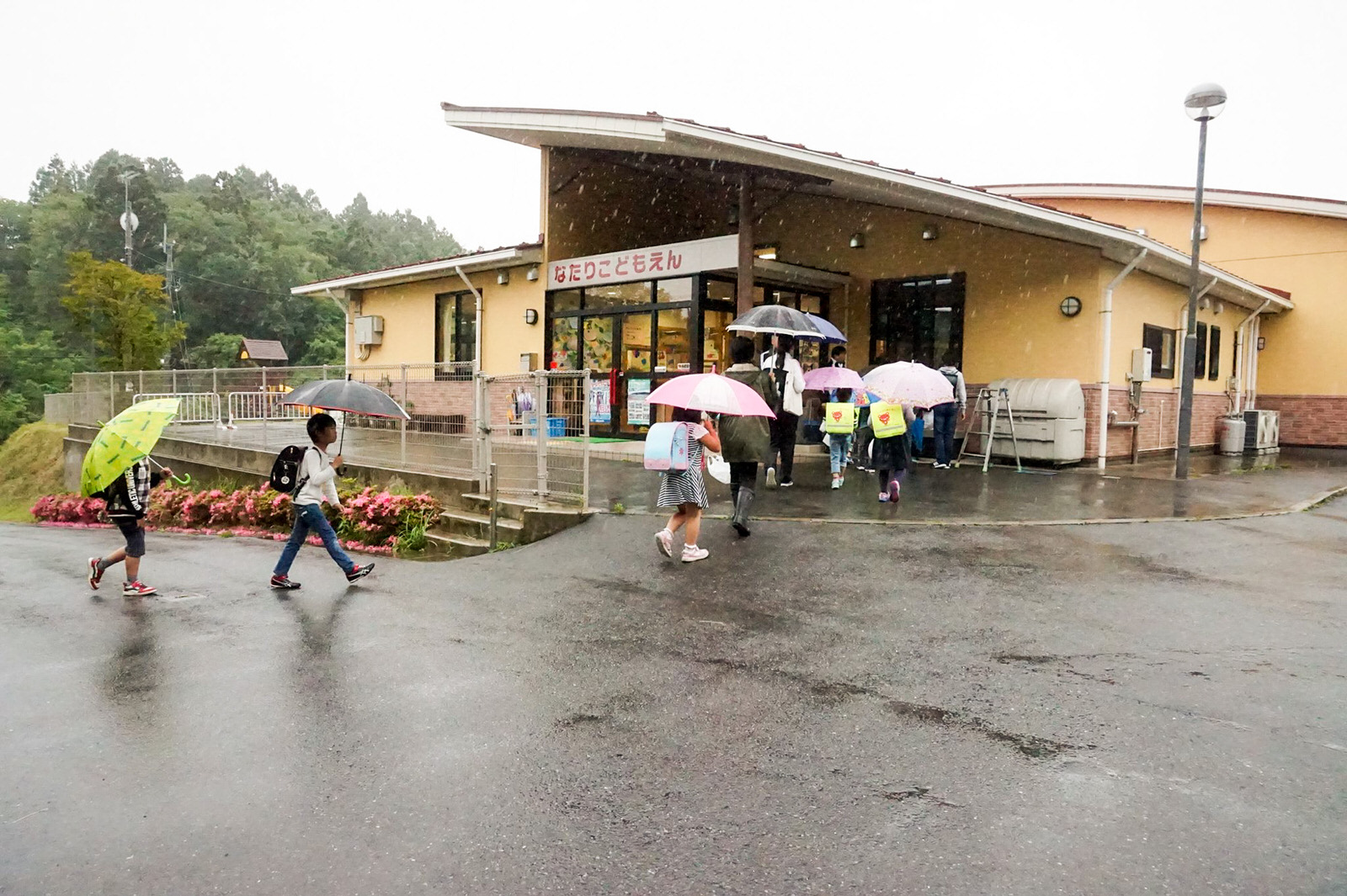 傘を差した子どもたちが、坂道を上がって避難場所の建物に入っていく様子の写真