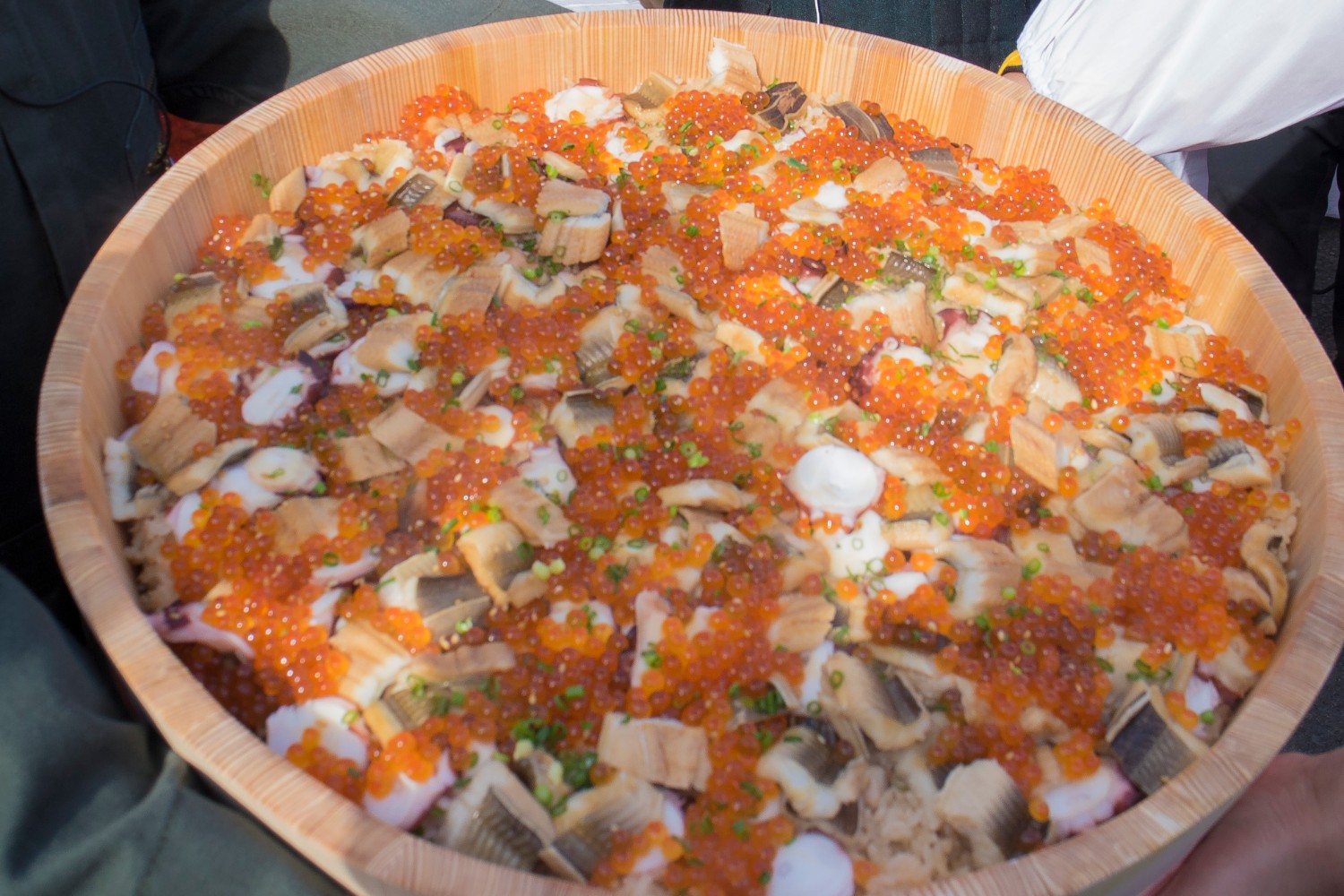 大きな木製の桶の中に、いくら、タコ、穴子、細かく刻んだネギなど色鮮やかな具材が敷き詰められた「さんこめし」が盛り付けられている様子を上から写した写真